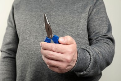 Photo of Man with needle nose pliers on light background, closeup