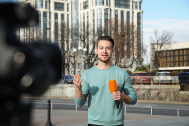 Young male journalist with microphone working on city street