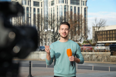 Photo of Young male journalist with microphone working on city street