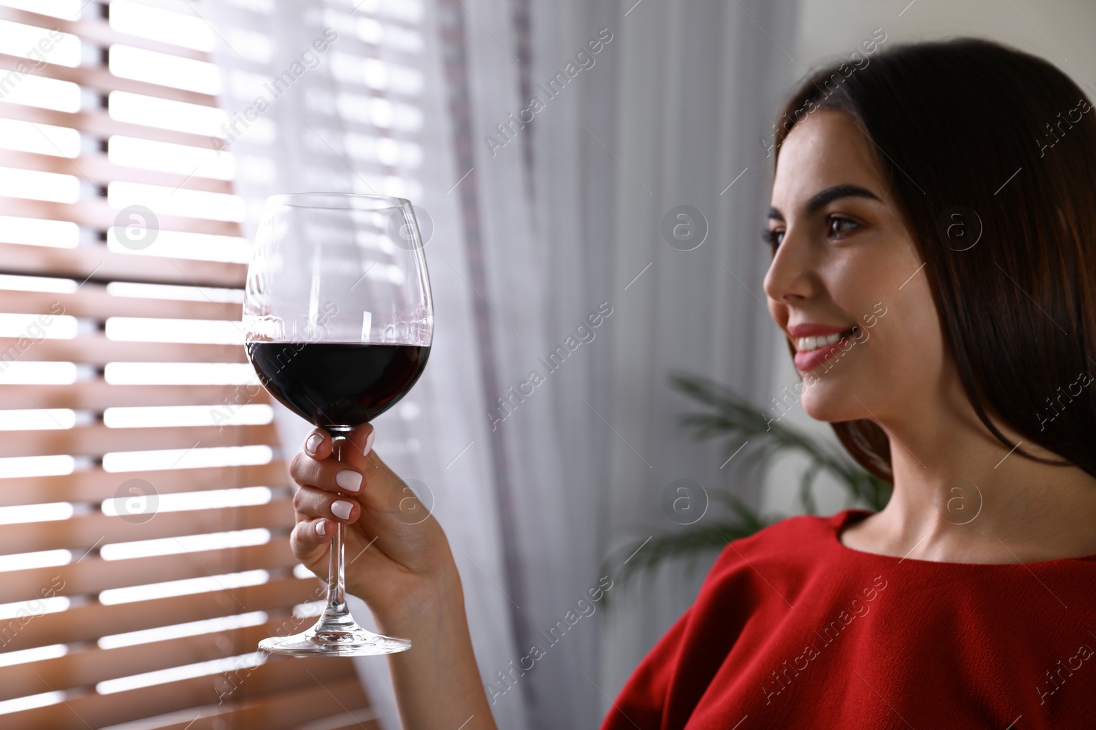 Photo of Beautiful young woman with glass of luxury red wine indoors. Space for text