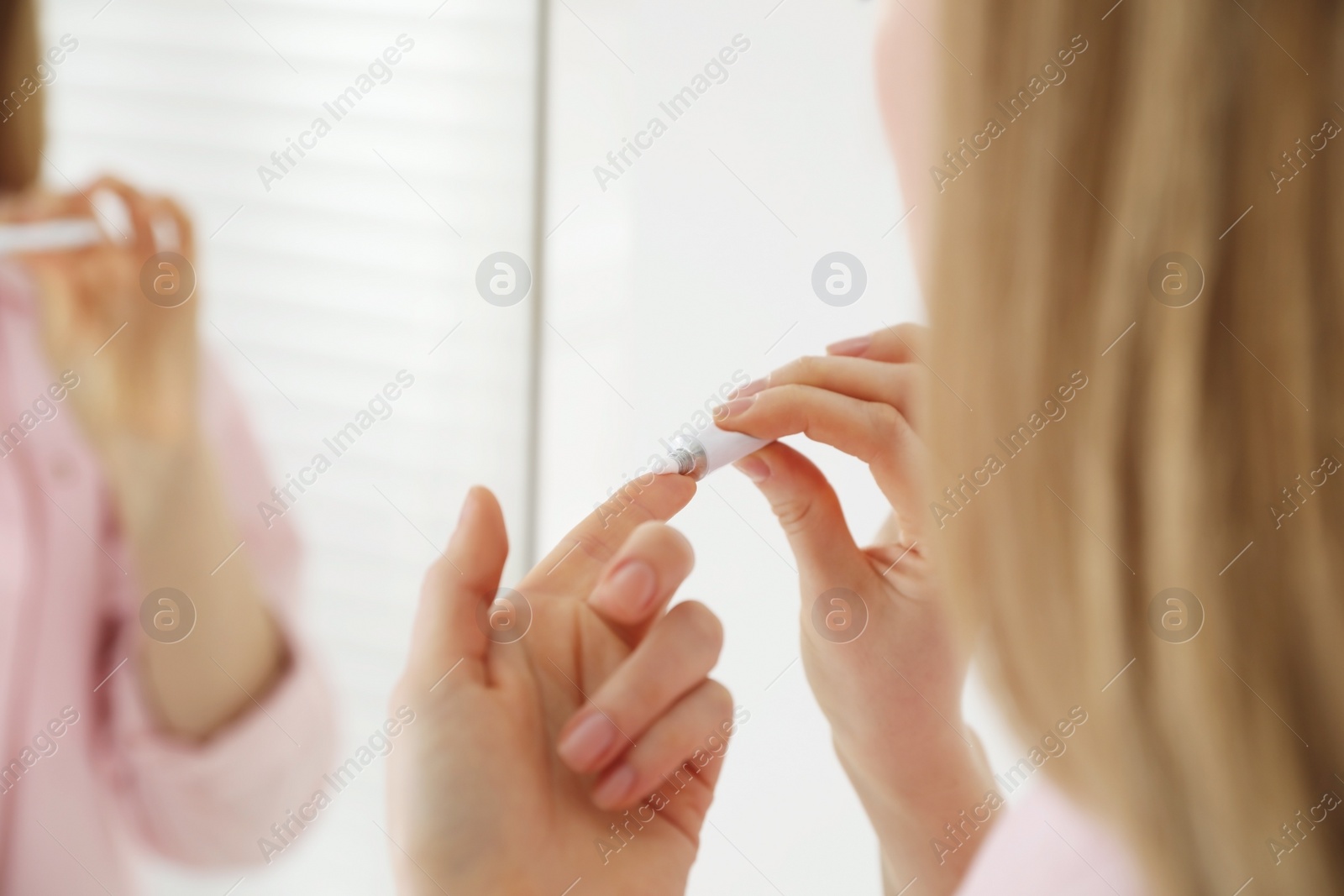 Photo of Woman with herpes applying cream on lips indoors, closeup