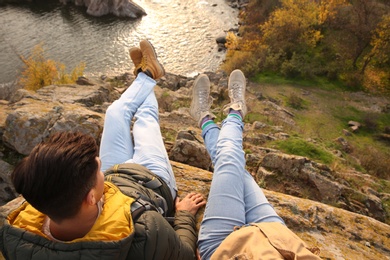Photo of Couple wearing stylish hiking boots sitting on steep cliff, above view