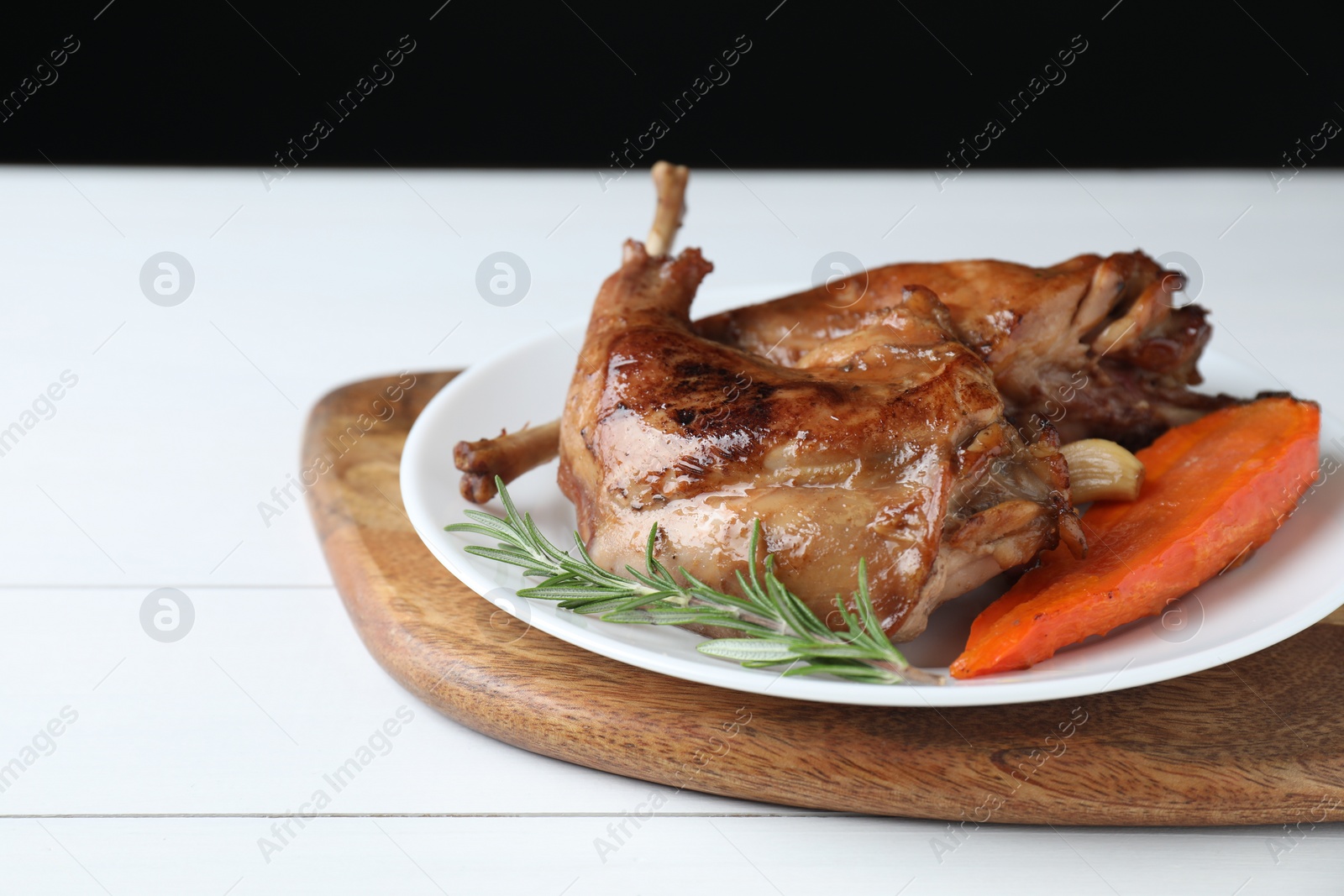 Photo of Tasty cooked rabbit meat with rosemary, garlic and carrot on white wooden table, closeup. Space for text