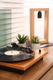 Photo of Stylish turntable with vinyl record on wooden chest of drawers indoors