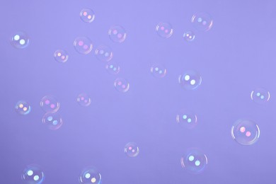 Photo of Many beautiful soap bubbles on violet background