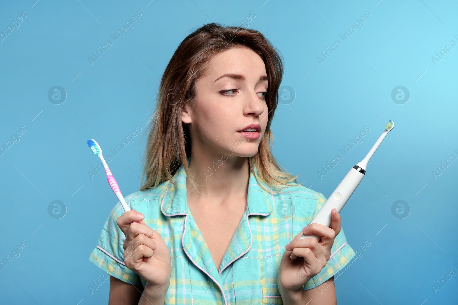 Photo of Young woman choosing between manual and electric toothbrushes on color background