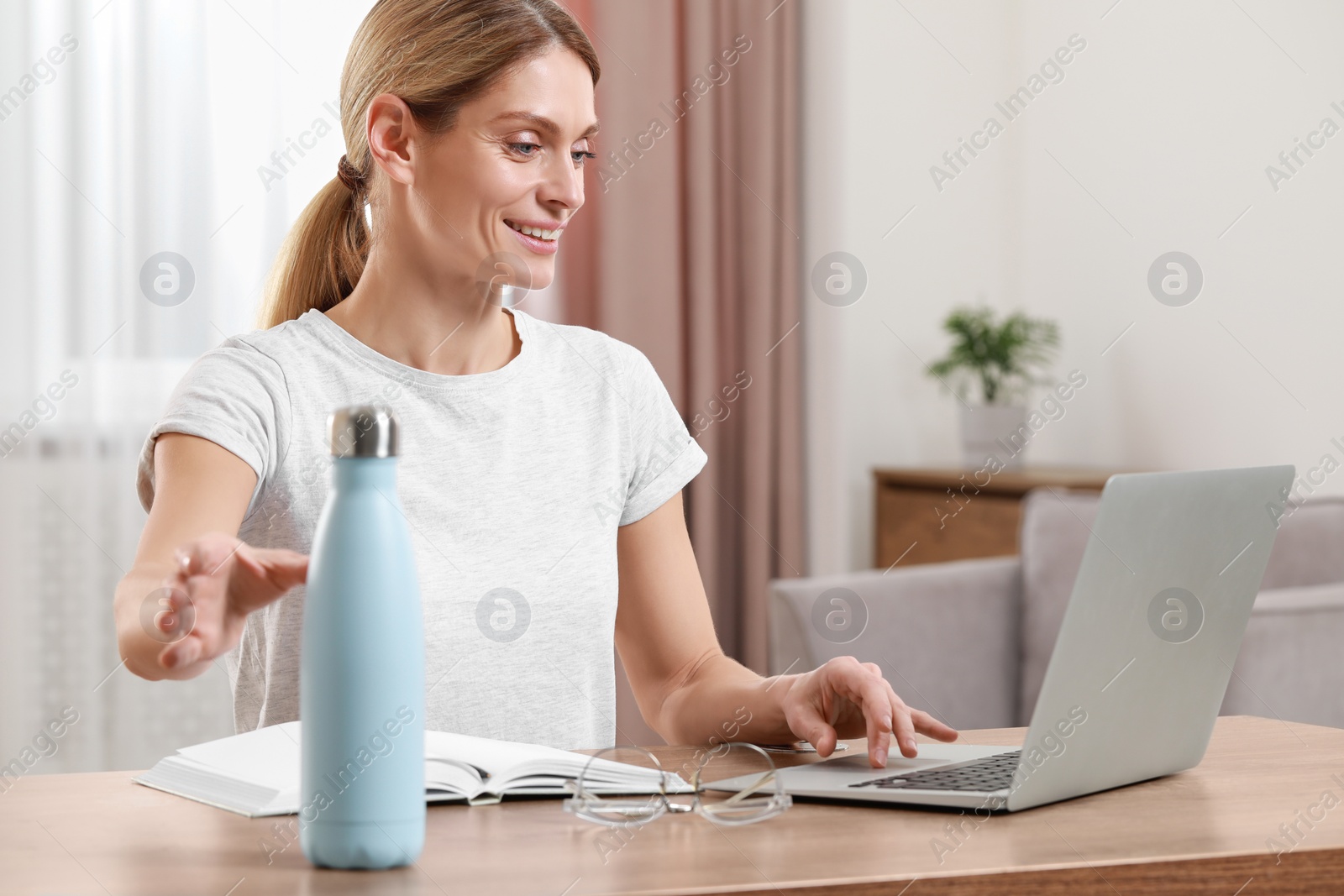 Photo of Woman taking thermo bottle at table indoors