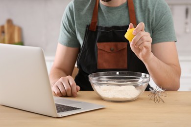 Photo of Man learning to cook with online video at wooden table in kitchen, closeup. Time for hobby