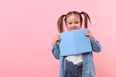 Photo of Cute little girl with book on pink background. Space for text