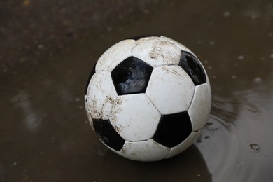 Photo of Dirty soccer ball near puddle outdoors, closeup