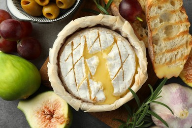 Tasty baked brie cheese and products on grey table, flat lay