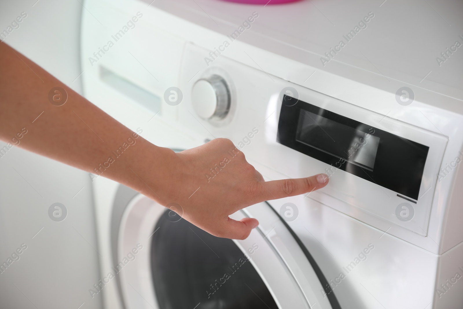 Photo of Woman pressing button on washing machine in bathroom, closeup