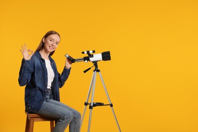 Photo of Happy astronomer with telescope showing OK gesture on orange background, space for text