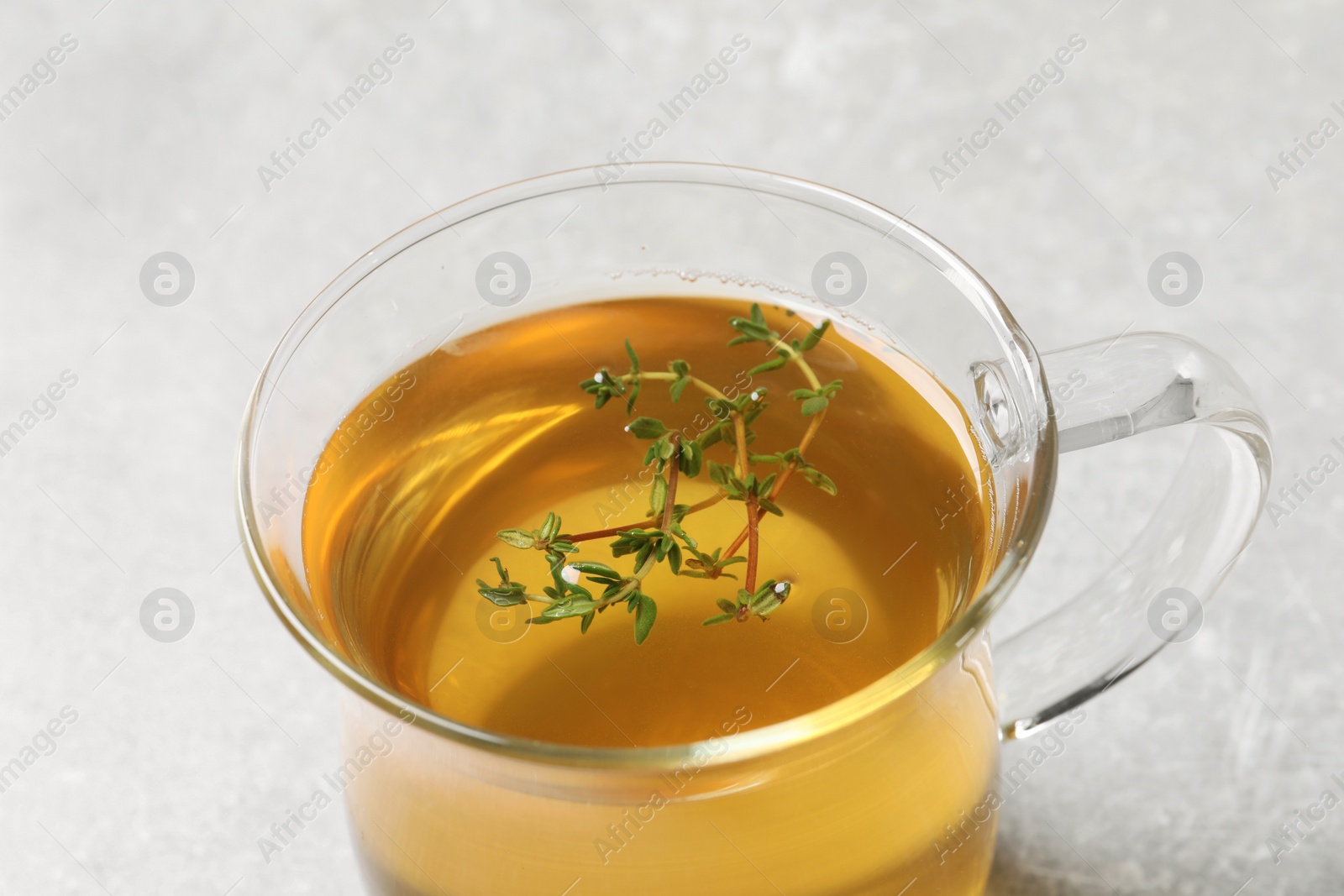 Photo of Glass cup of aromatic herbal tea with thyme on light grey table, closeup