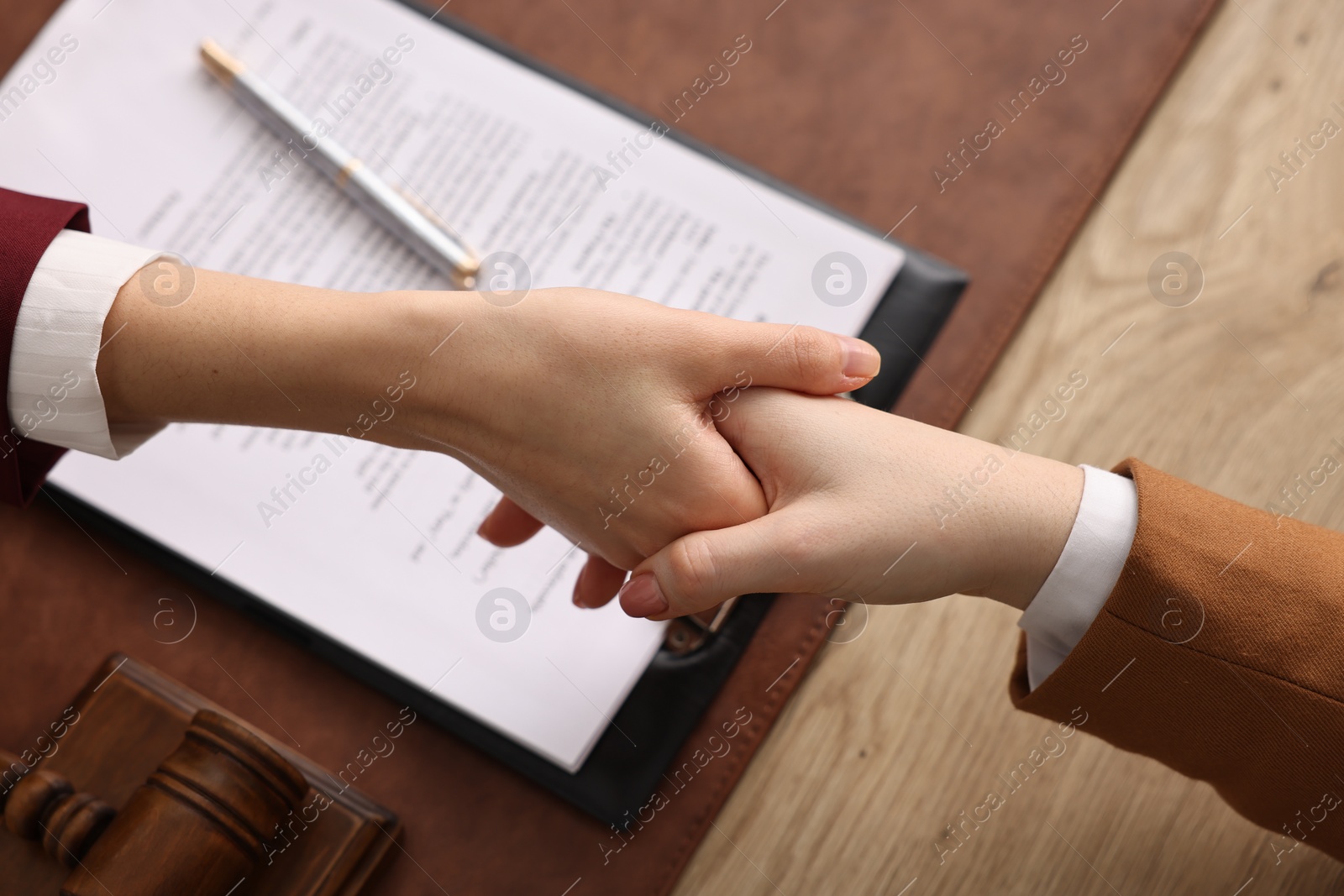 Photo of Notary shaking hands with client at wooden table, closeup