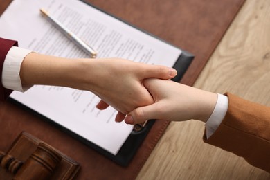 Photo of Notary shaking hands with client at wooden table, closeup