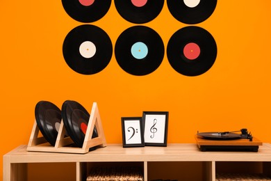 Photo of Vinyl records and player on wooden cabinet near orange wall