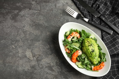 Delicious avocado salad with shrimps in bowl on grey table, flat lay. Space for text