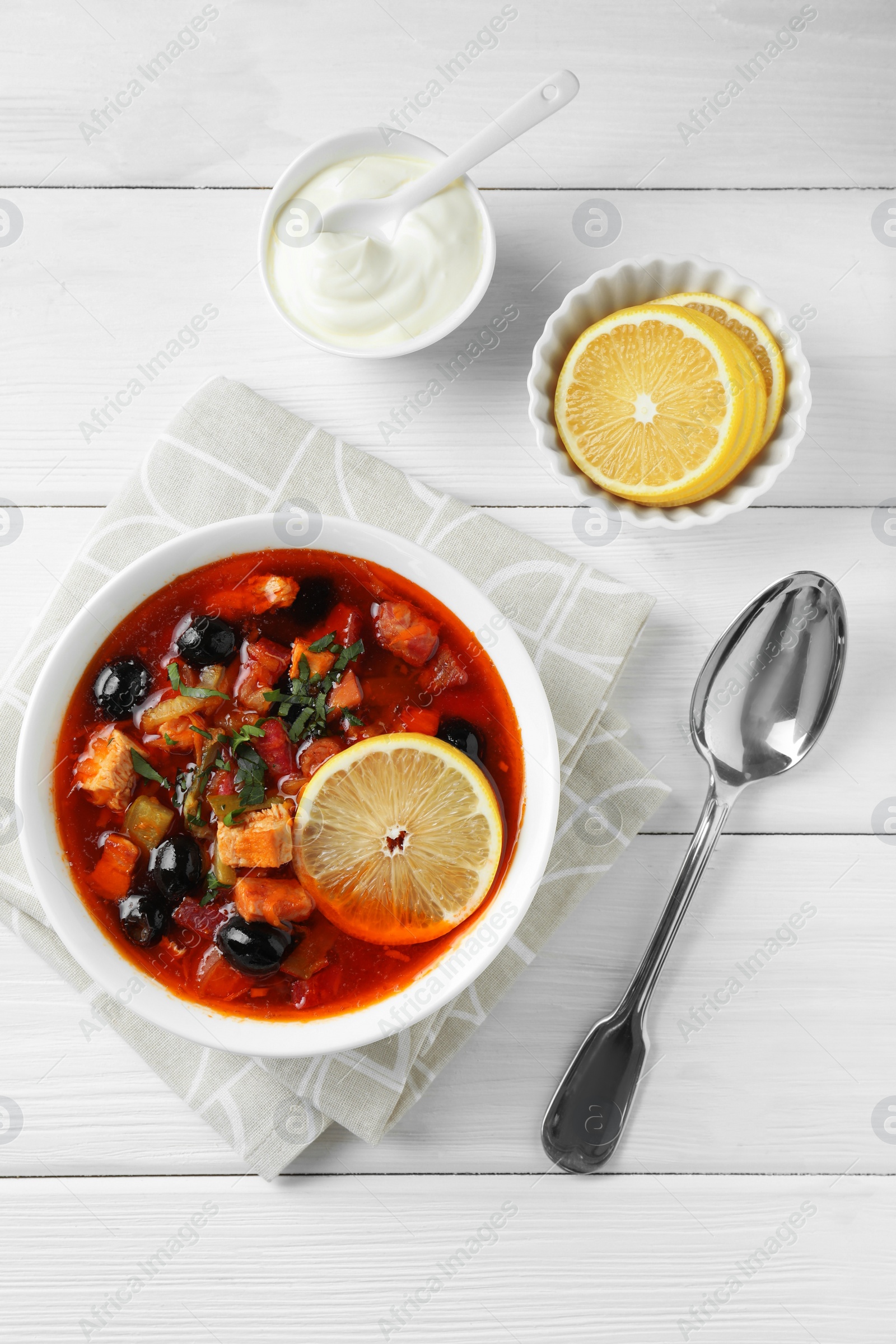 Photo of Meat solyanka soup with sausages, olives and vegetables served on white wooden table, flat lay