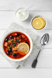 Meat solyanka soup with sausages, olives and vegetables served on white wooden table, flat lay