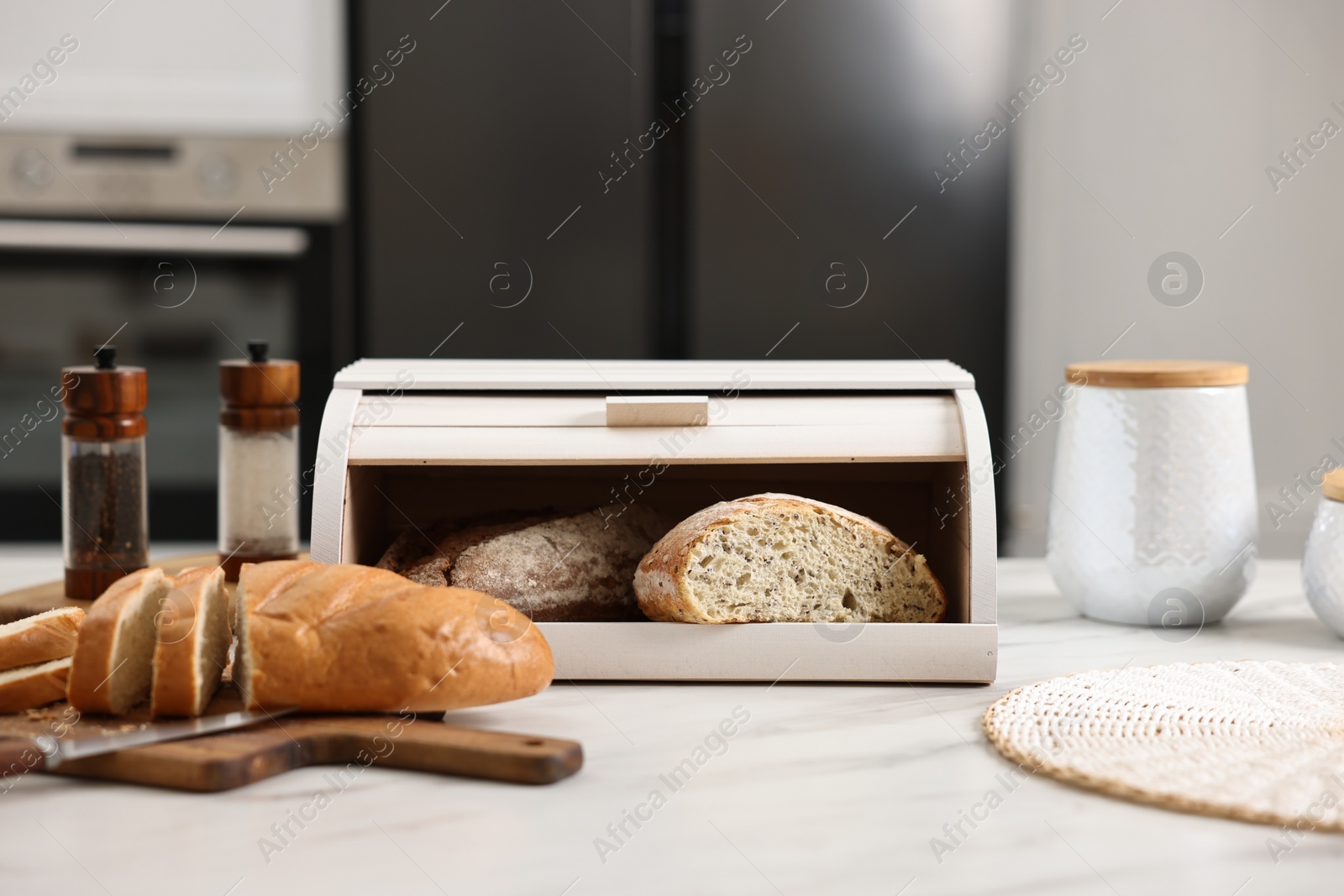 Photo of Wooden bread basket with freshly baked loaves and knife on white marble table in kitchen