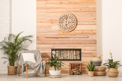 Beautiful plants and armchair near wooden wall. Stylish interior design