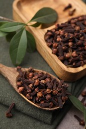 Photo of Wooden tray with aromatic cloves, spoon and green leaves on table, closeup