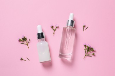 Bottles of cosmetic serums and beautiful flowers on pink background, flat lay