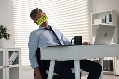 Man with fake eyes painted on sticky notes snoozing at workplace in office