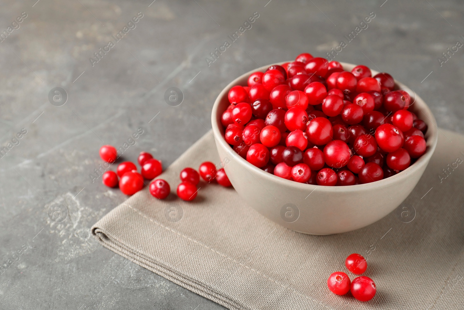 Photo of Cranberries in bowl on light grey table, closeup. Space for text