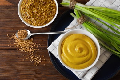 Photo of Delicious whole grain mustard, seeds and fresh green onion on wooden table, flat lay