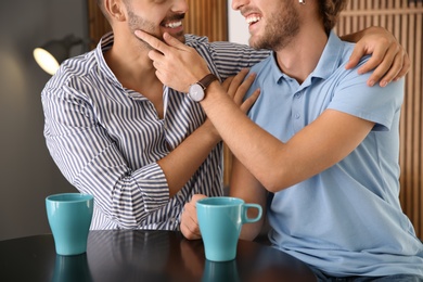 Happy gay couple with coffee at table indoors, closeup