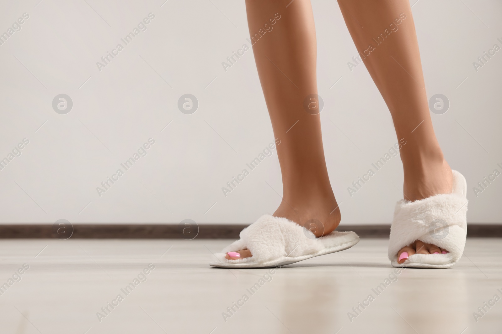 Photo of Woman wearing white soft slippers indoors, closeup. Space for text