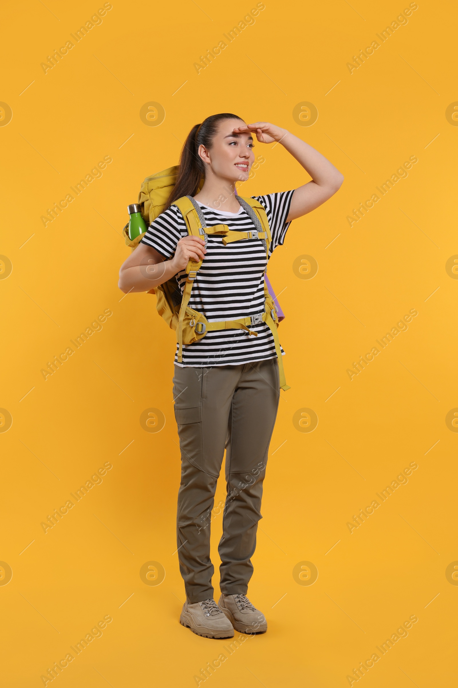 Photo of Smiling young woman with backpack on orange background. Active tourism