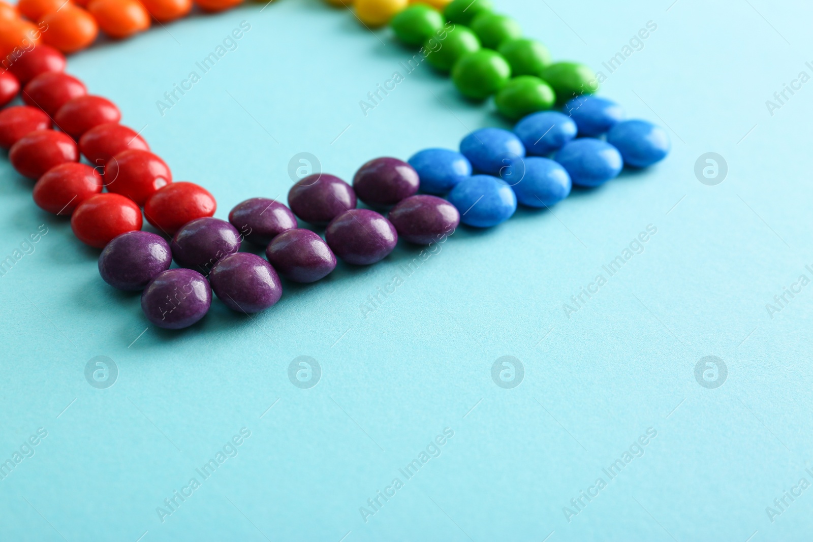 Photo of Colorful delicious glazed candies on light blue background, closeup. Space for text