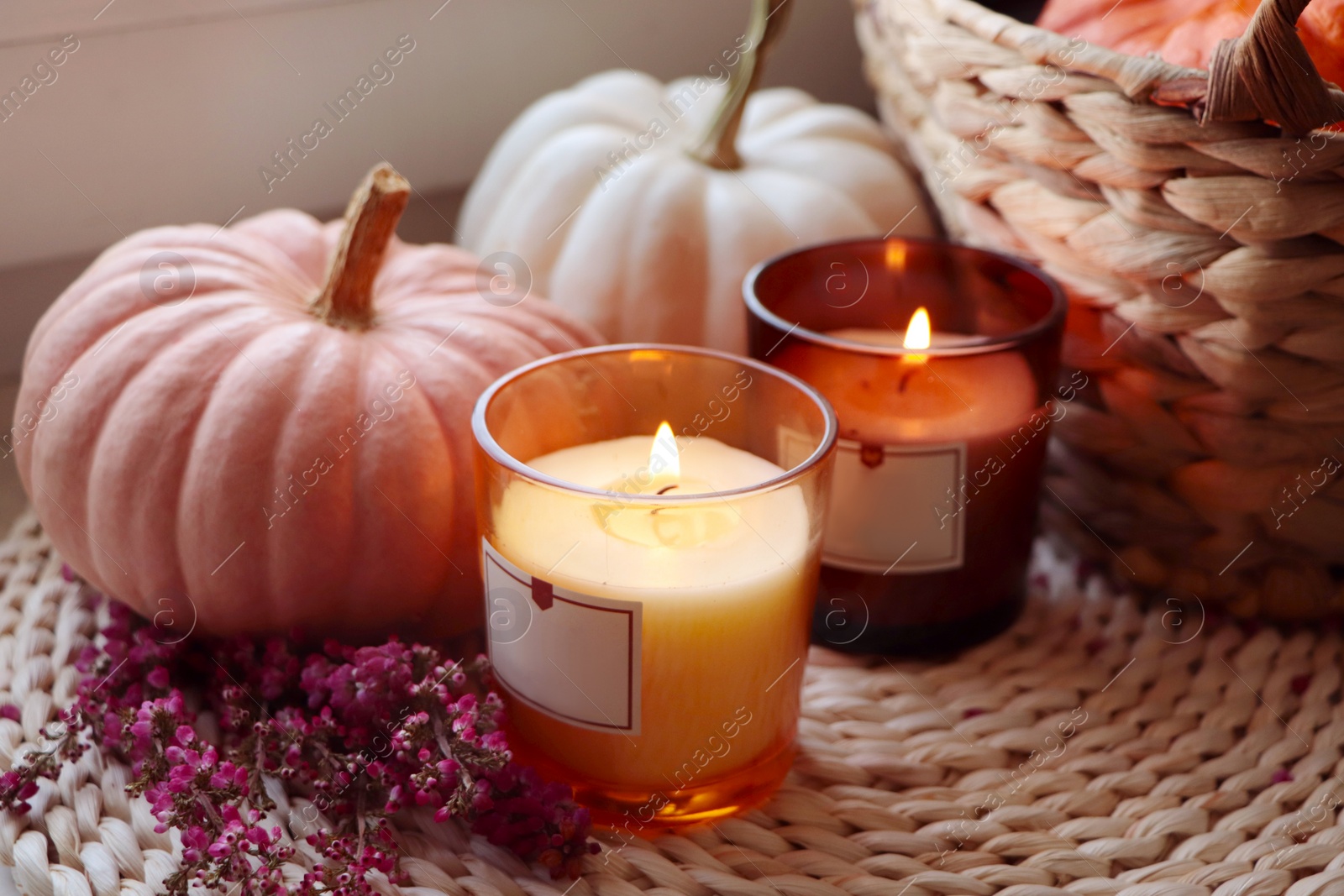 Photo of Basket, beautiful heather flowers, pumpkins and burning candles on wicker mat, closeup