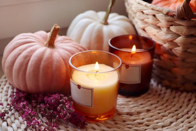 Basket, beautiful heather flowers, pumpkins and burning candles on wicker mat, closeup