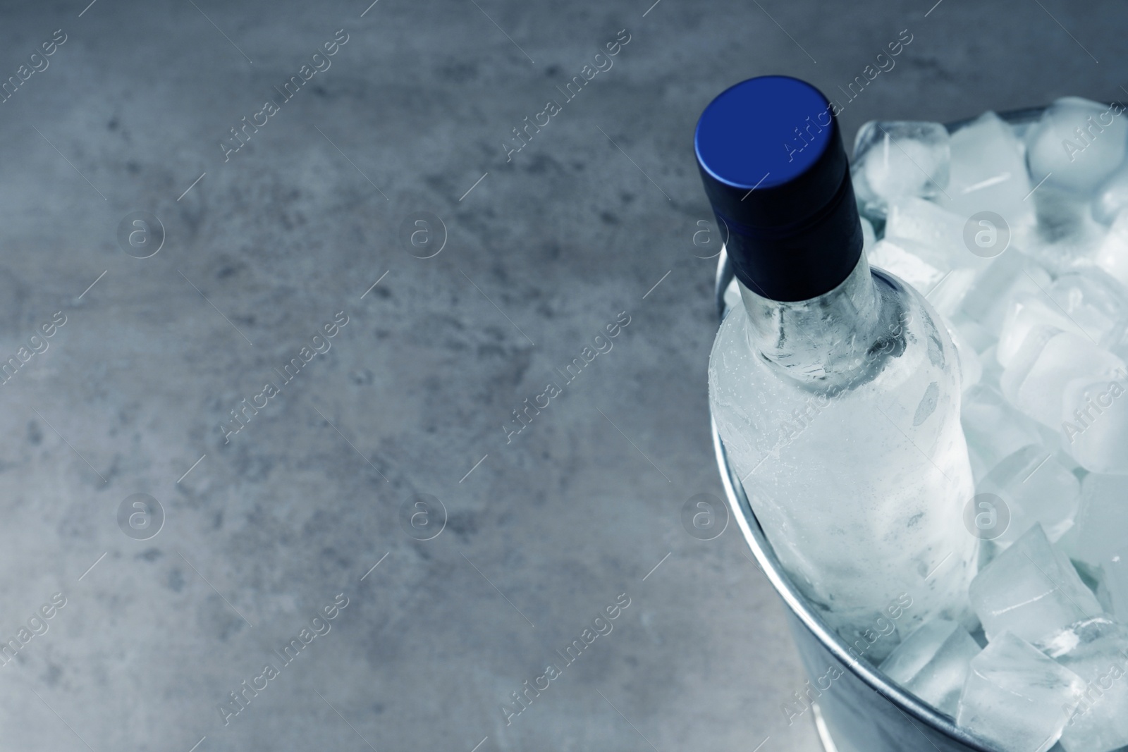 Photo of Bottle of vodka in metal bucket with ice on grey table, above view. Space for text