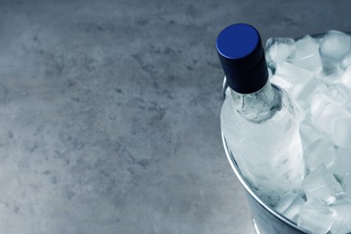 Photo of Bottlevodka in metal bucket with ice on grey table, above view. Space for text