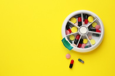 Photo of Plastic box with different pills on yellow background, flat lay. Space for text