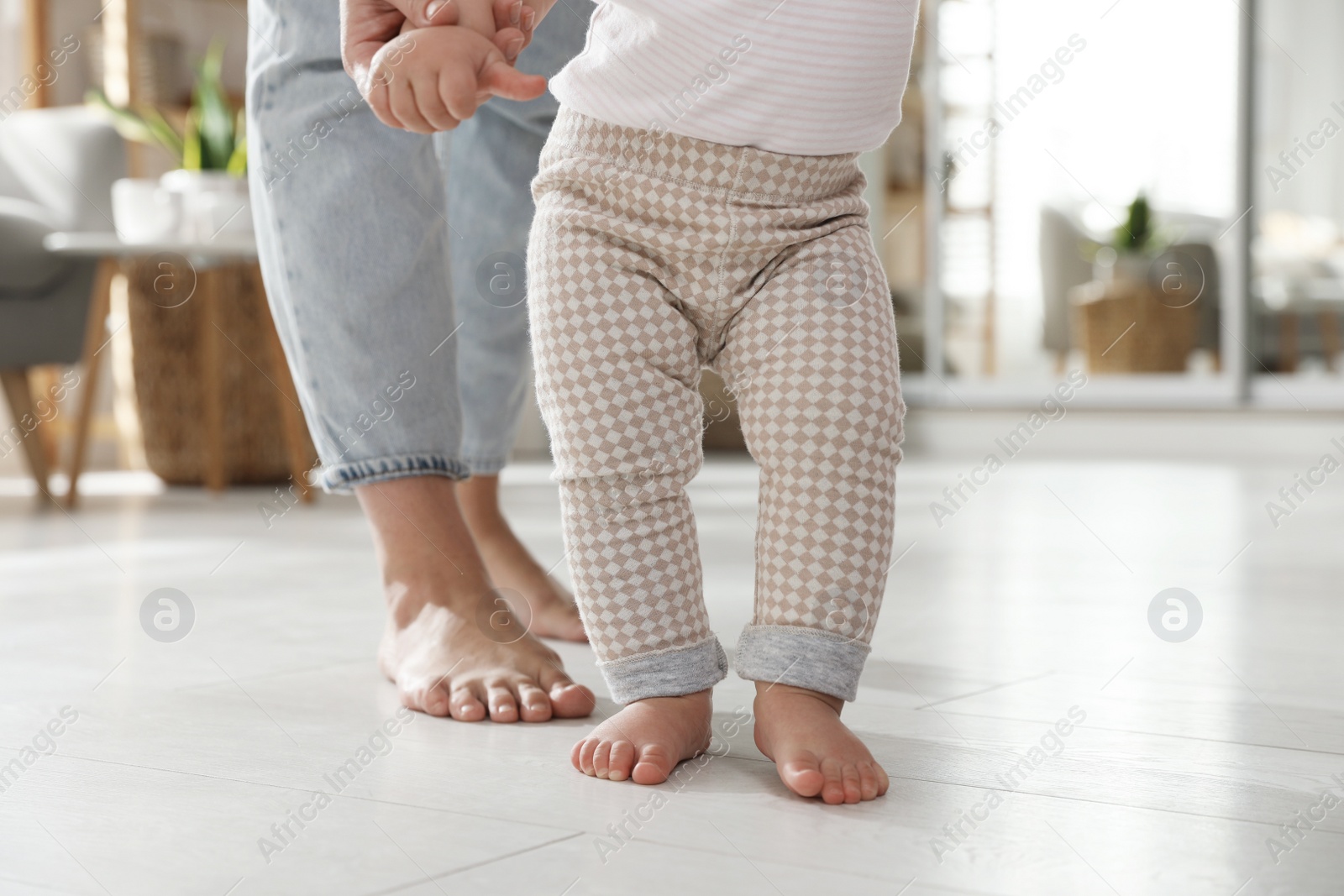 Photo of Mother supporting her baby daughter while she learning to walk at home, closeup