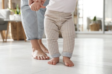 Photo of Mother supporting her baby daughter while she learning to walk at home, closeup