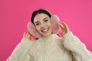 Photo of Beautiful young woman wearing earmuffs on pink background