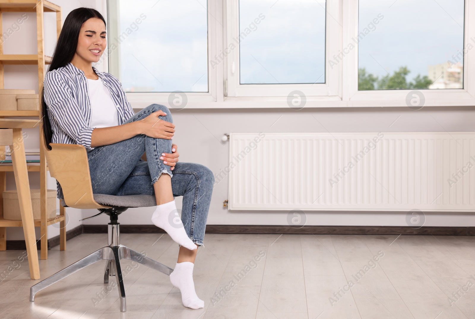 Photo of Woman suffering from leg pain on chair at home, space for text