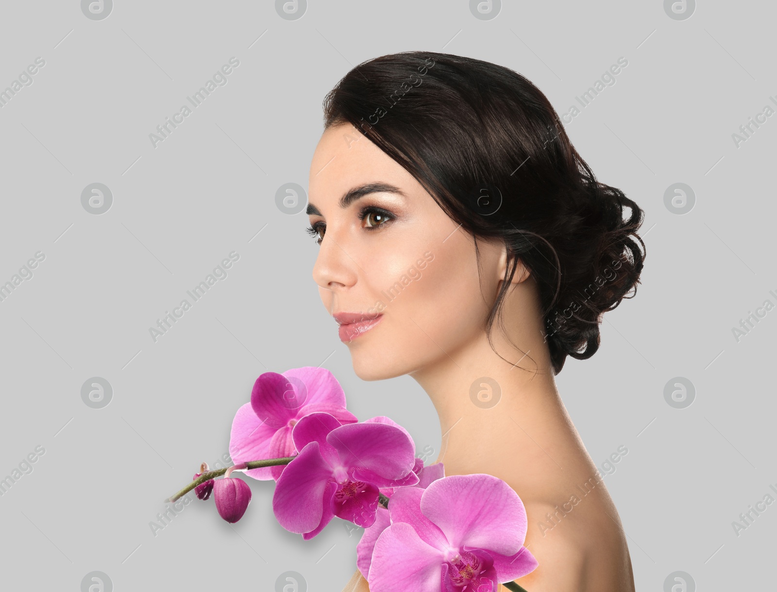 Image of Beautiful young woman and orchid flowers on light background. Spa portrait