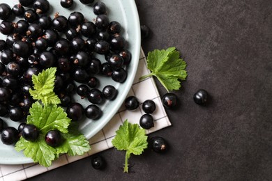 Plate with ripe blackcurrants and leaves on grey background, flat lay. Space for text