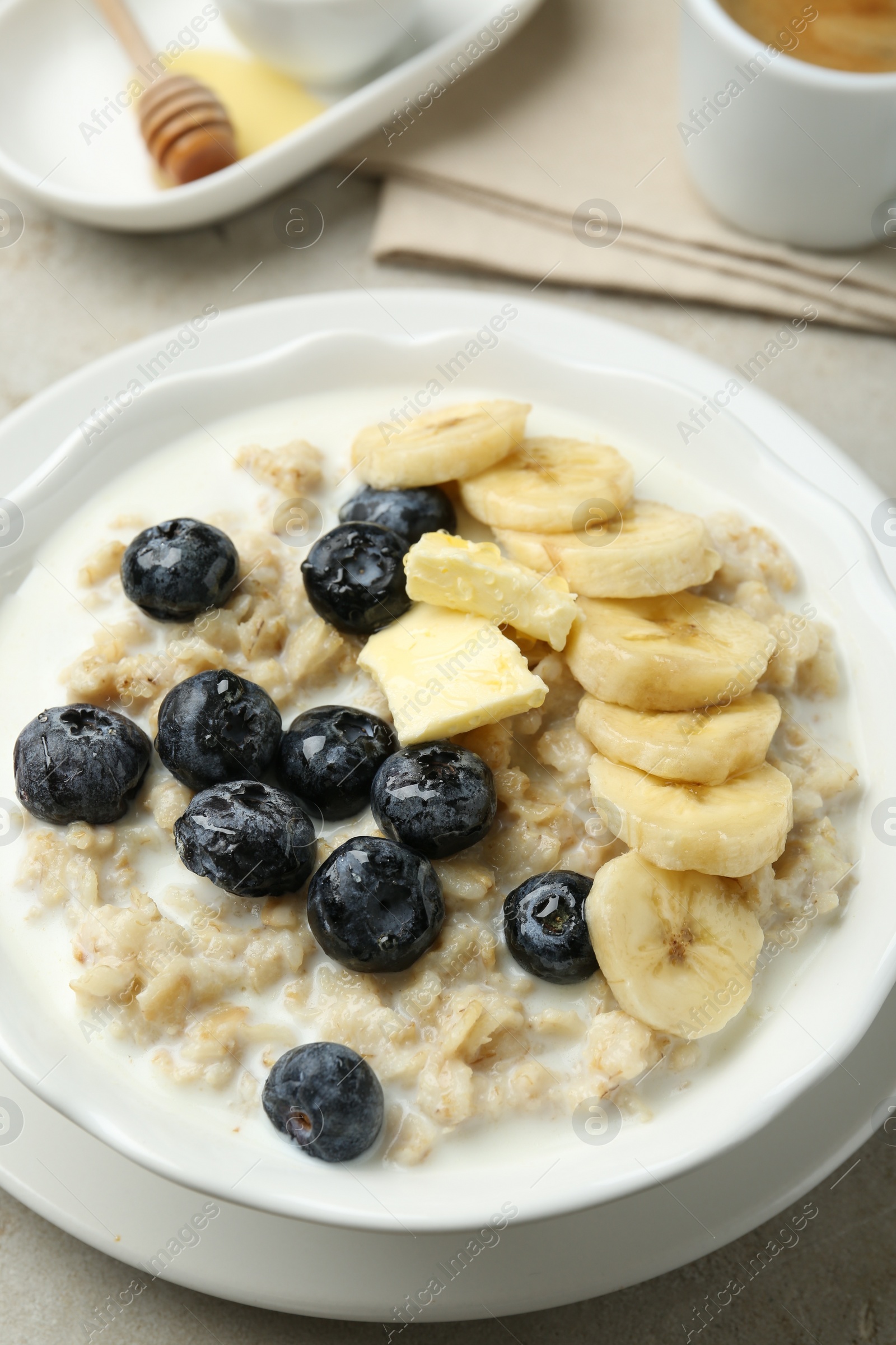 Photo of Tasty oatmeal with banana, blueberries, butter and milk served in bowl on light grey table, closeup