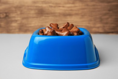 Photo of Blue bowl with bone shaped dog cookies on light table, closeup