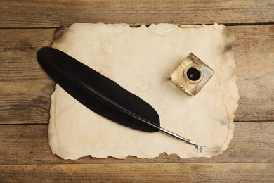 Photo of Feather pen, inkwell and parchment on wooden table, top view