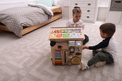 Photo of Little boy and girl playing with busy board house on floor in room